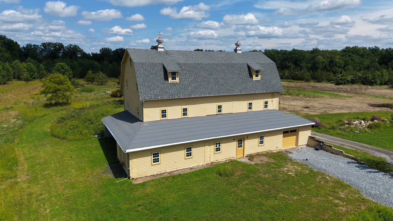 An aerial view of the yellow barn that will become Lumina Movement Studio, standing in open green fields.